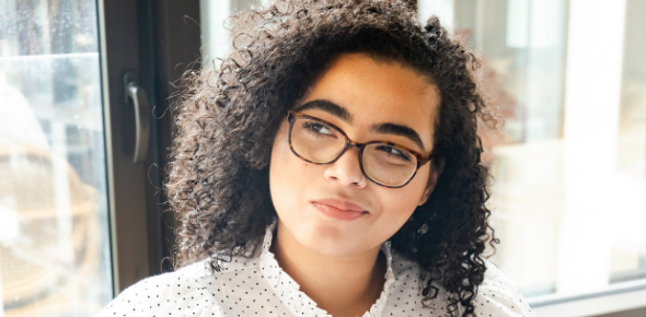 Young woman with curly, textured hair and glasses looking to the side like she's doubtful or has a question